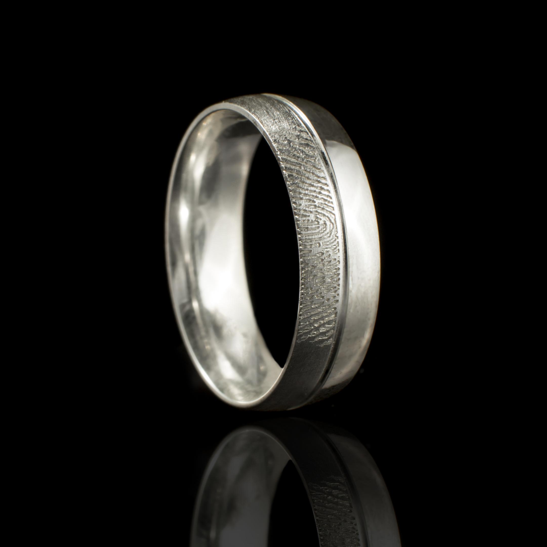 "Handgemaakte zilveren ring met subtiele vingerafdrukgravure aan de buitenkant, gecombineerd met een matte en gepolijste afwerking. Een elegant en gepersonaliseerd sieraad.